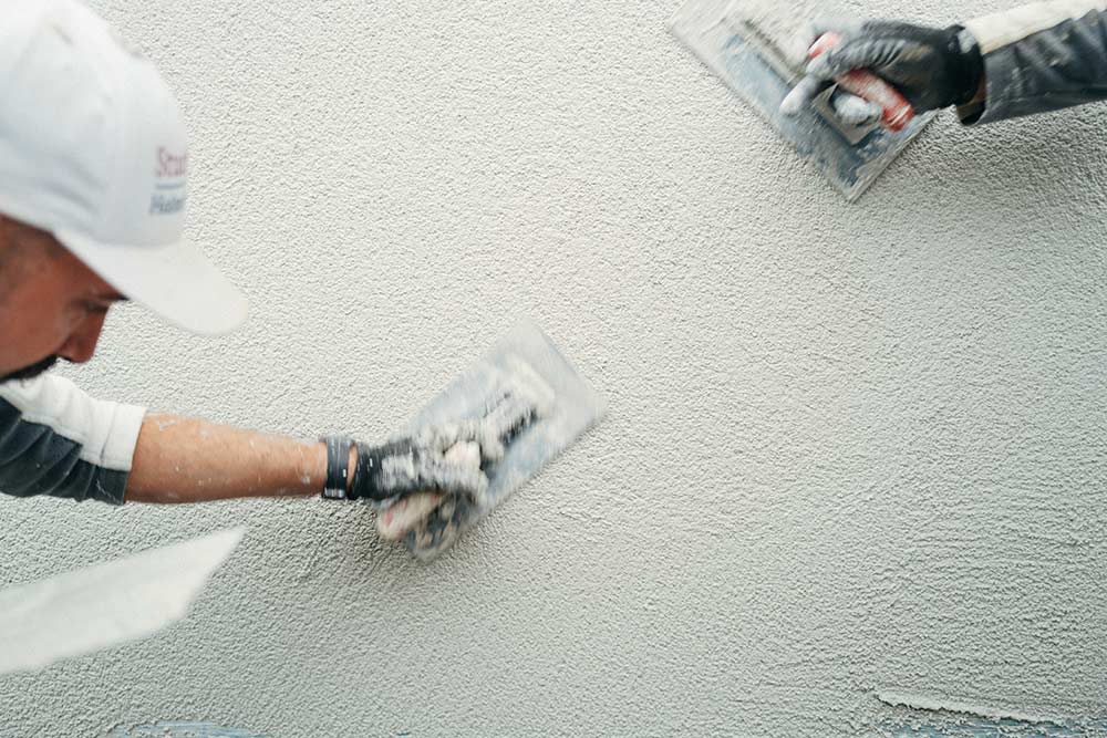 Detailbild den Händen und Kellen von zwei Stuckateuren beim Verputzen einer Außenwand