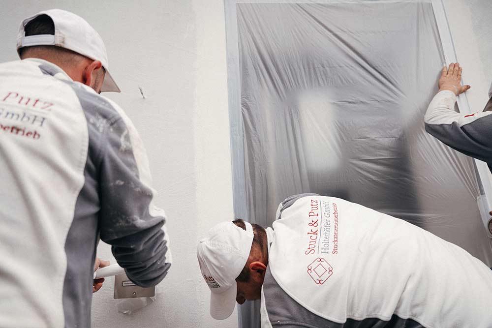 Stuckateurteam klebt Teile einer Wand ab, um daran zu arbeiten